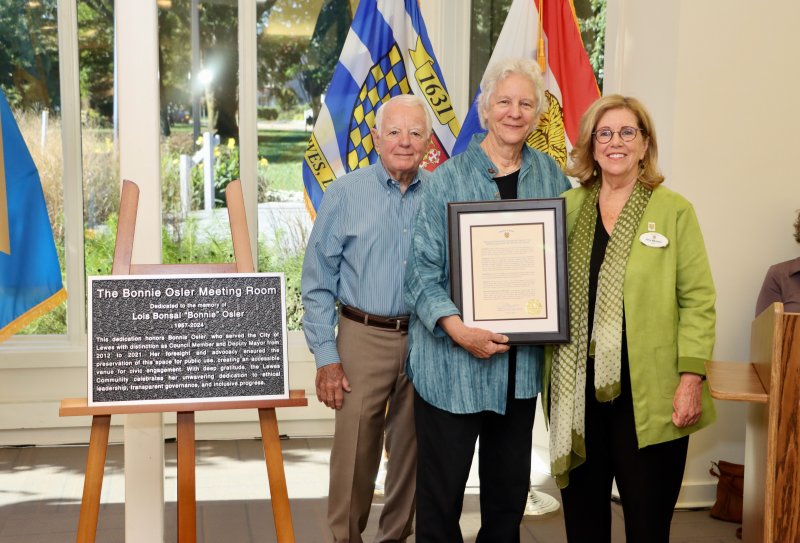 The City of Lewes dedicated its meeting room in the Margaret Rollins Community Center as the Bonnie Osler Meeting Room Oct. 9. The city also recognized Oct. 9 as Bonnie Osler Day. Osler served on city council for eight years. She died in 2024. Shown are (l-r) Dennis Reardon, former Lewes city councilman and Osler’s friend; Brook Hedge, Osler’s spouse, holding the Bonnie Osler Day proclamation; and Lewes Mayor Amy Marasco. The plaque that now hangs in the room is on the left. BILL SHULL PHOTOS